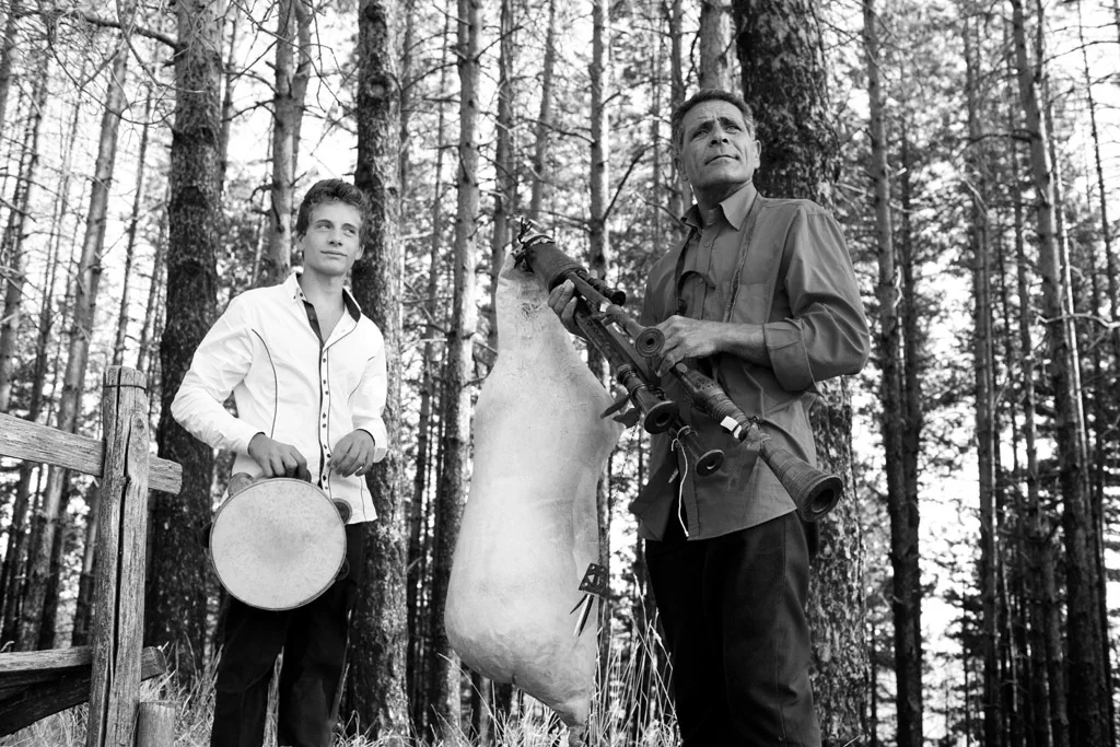 Two men making a drum among pine trees, stretching the skin over the frame