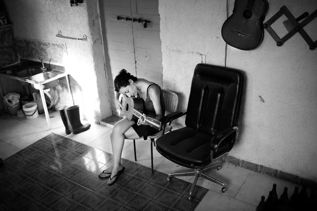 Woman playing guitar alone in a bare room, an office chair beside her