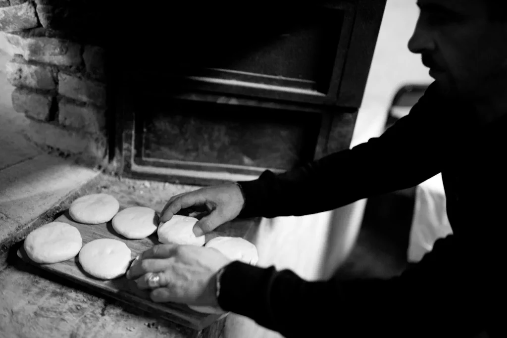 Hands laying rounds of dough into a wood-fired oven