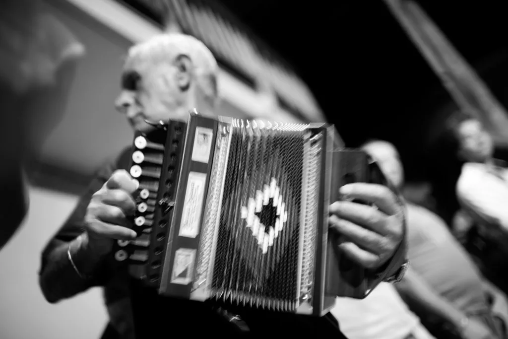 Elderly man playing a diatonic accordion in the middle of a crowd