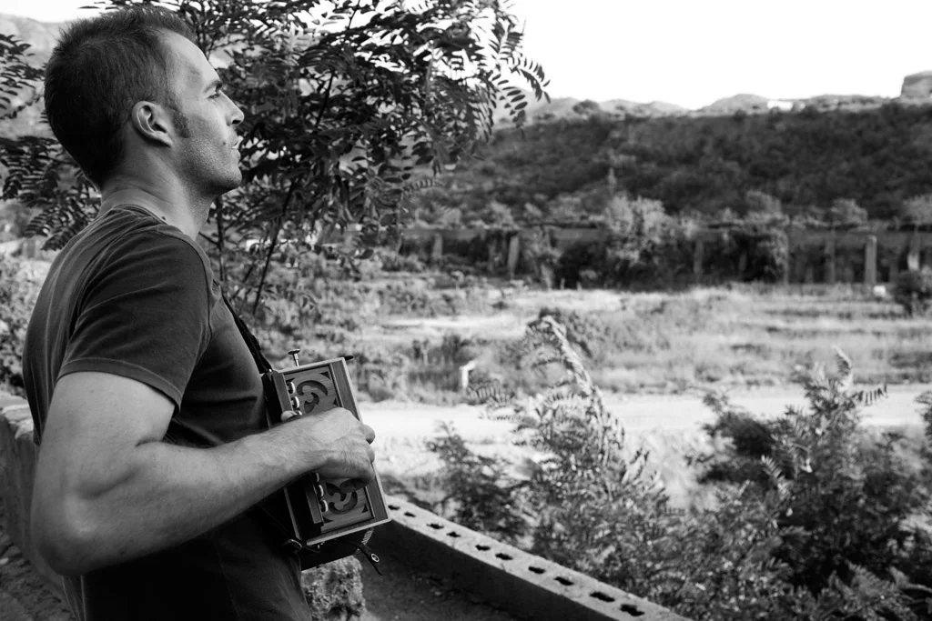 Man holding an accordion, looking out over a wide valley