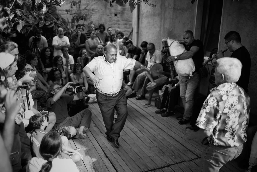 Man dancing on a wooden stage encircled by seated onlookers