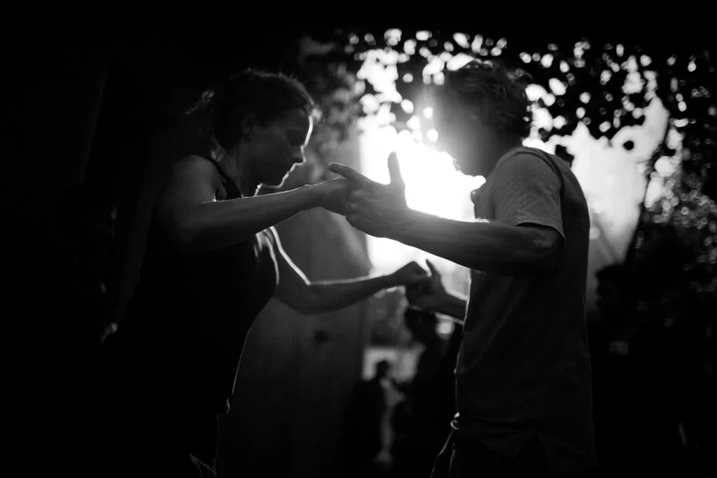 Two dancers holding hands against the light at night