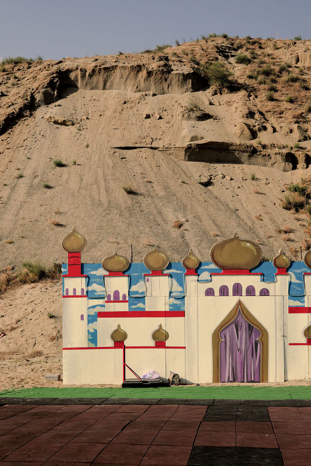 A painted stage flat in the shape of an oriental castle at the foot of an eroded earth slope