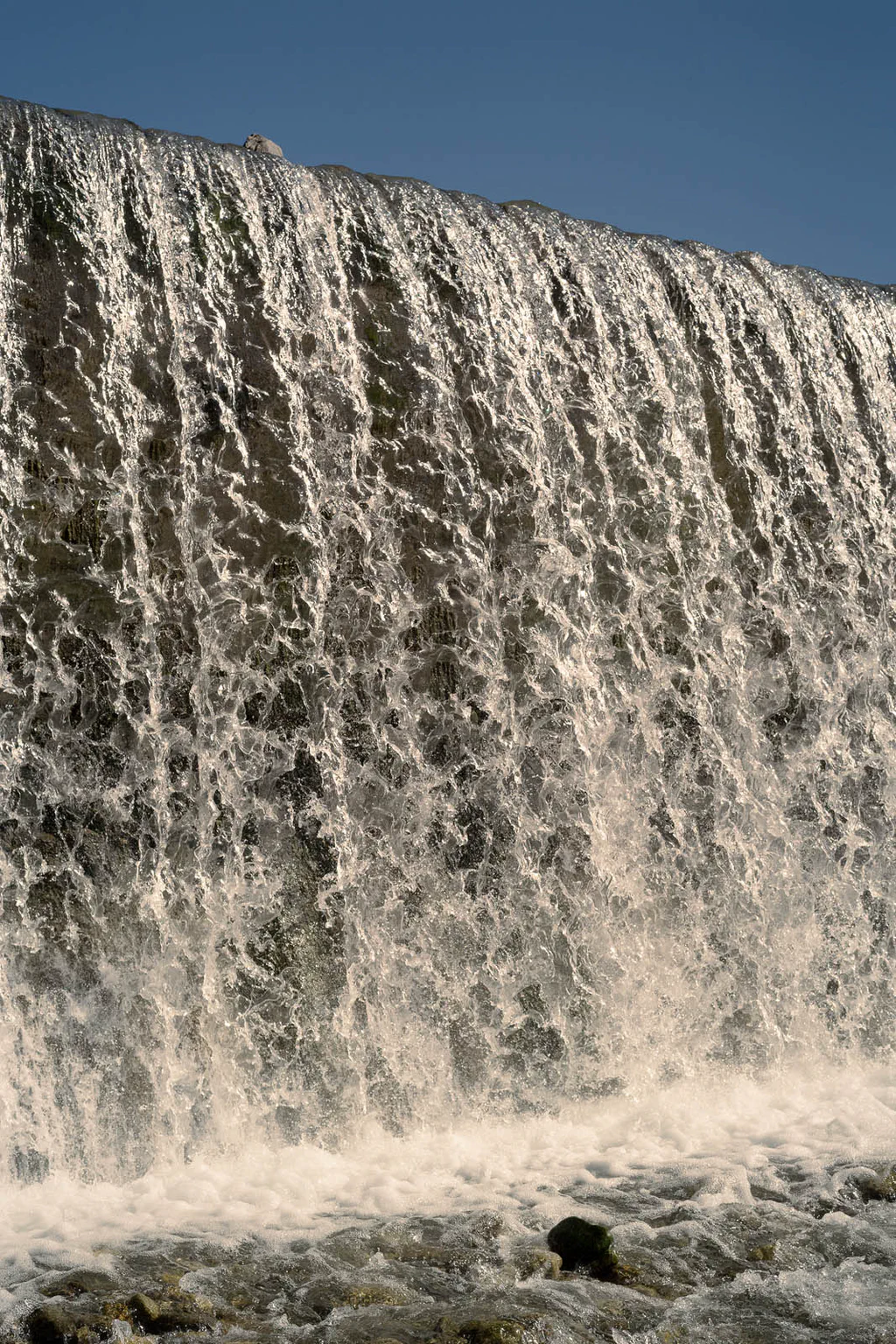 Water pouring over the lip of a weir into white foam