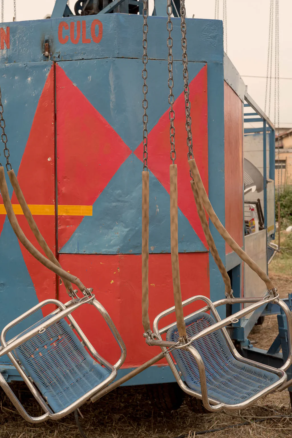 Fairground swing ride painted with red and blue diamonds, its seats hanging still