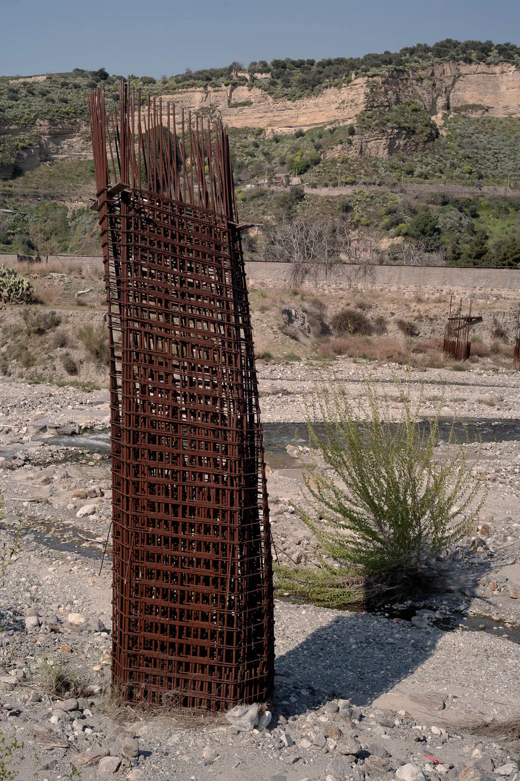 Roll of rusted reinforcement mesh left standing in a dry riverbed