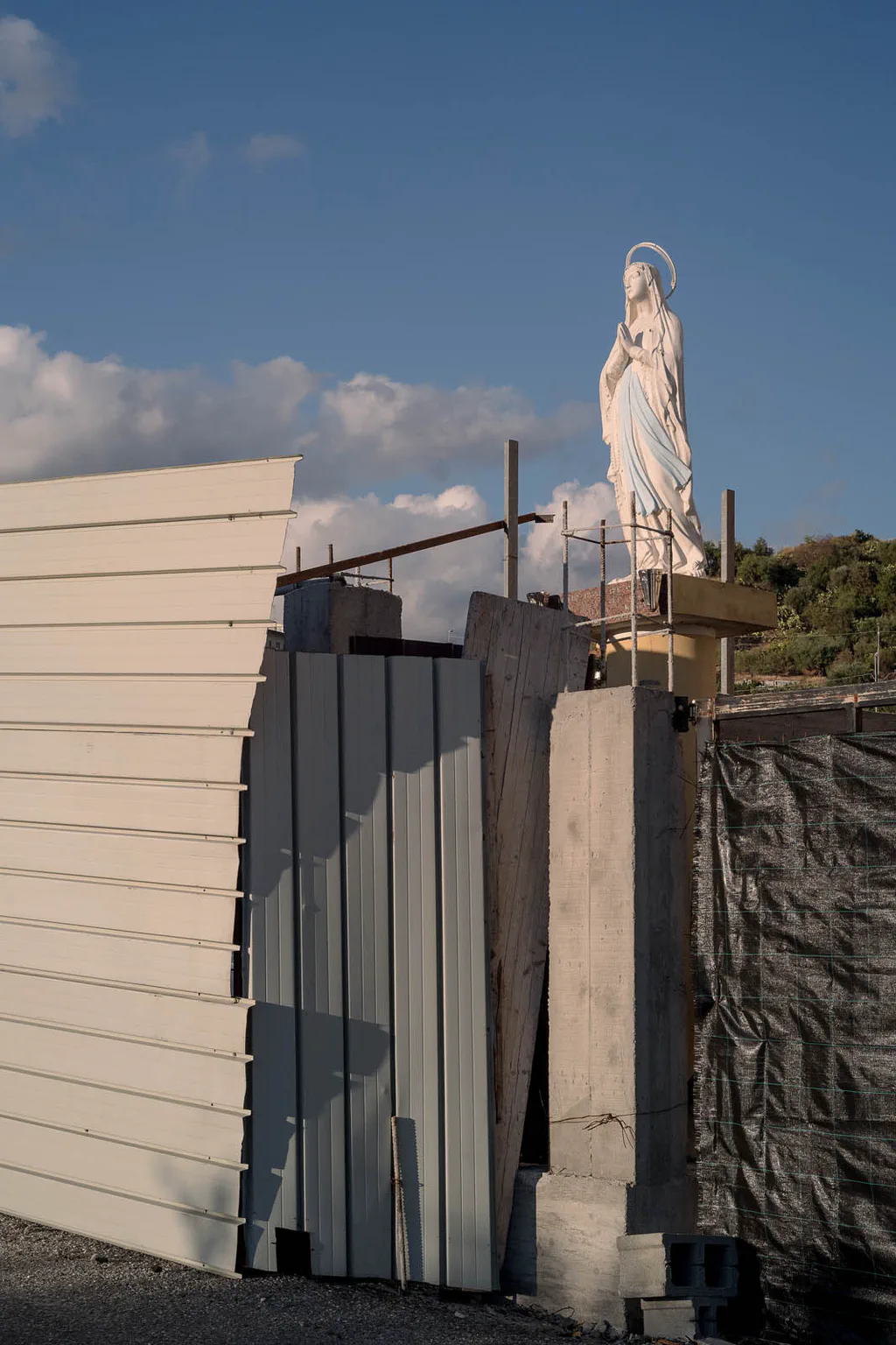 Statue of the Virgin on a makeshift plinth above a fence of mismatched panels