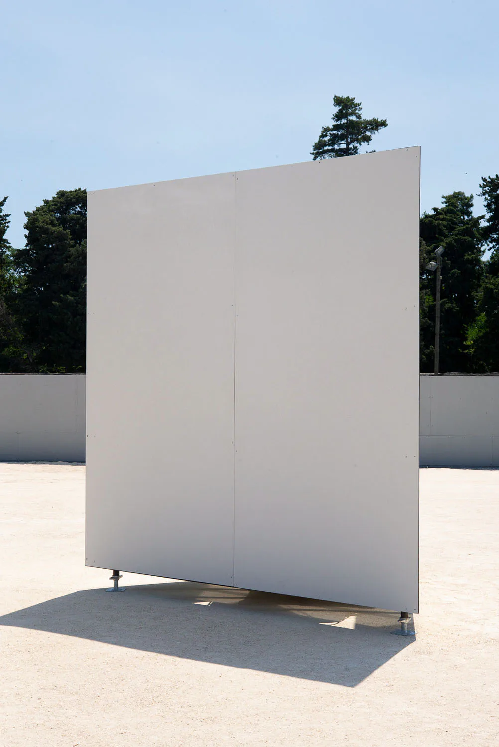 Blank white panel standing upright on an empty concrete forecourt, trees behind